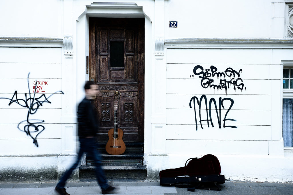 Gitarrist läuft vor Haus entlang und Gitarre lehnt an der Tür