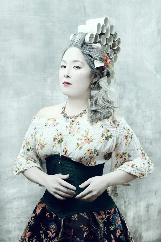 Asiatische Frau in barockem Kostüm mit Toilettenpapier im Haar